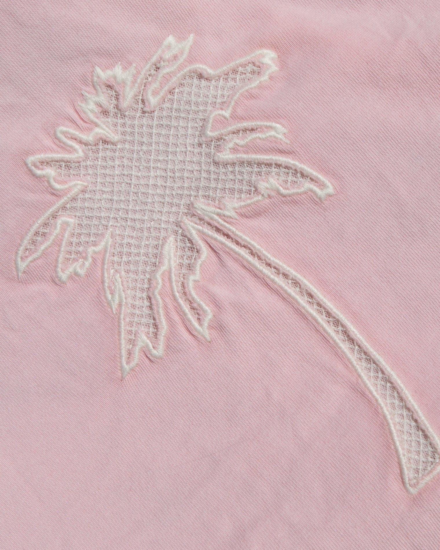 A close-up of a light pink fabric featuring a white embroidered palm tree motif.