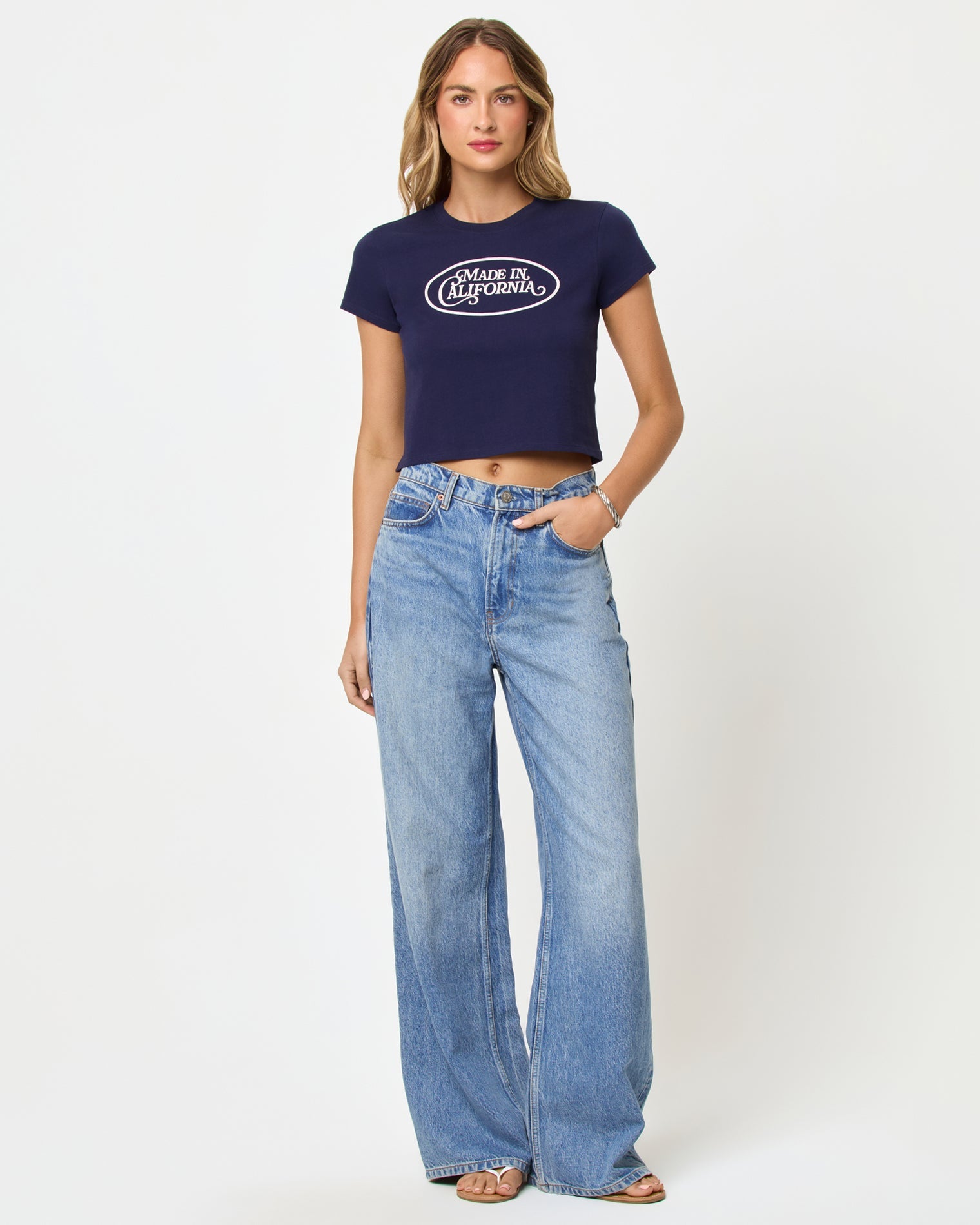 Front view of model wearing the LSPACE Merci Baby Tee in made in California midnight blue, a cropped navy fitted tee with a white graphic print on the chest.