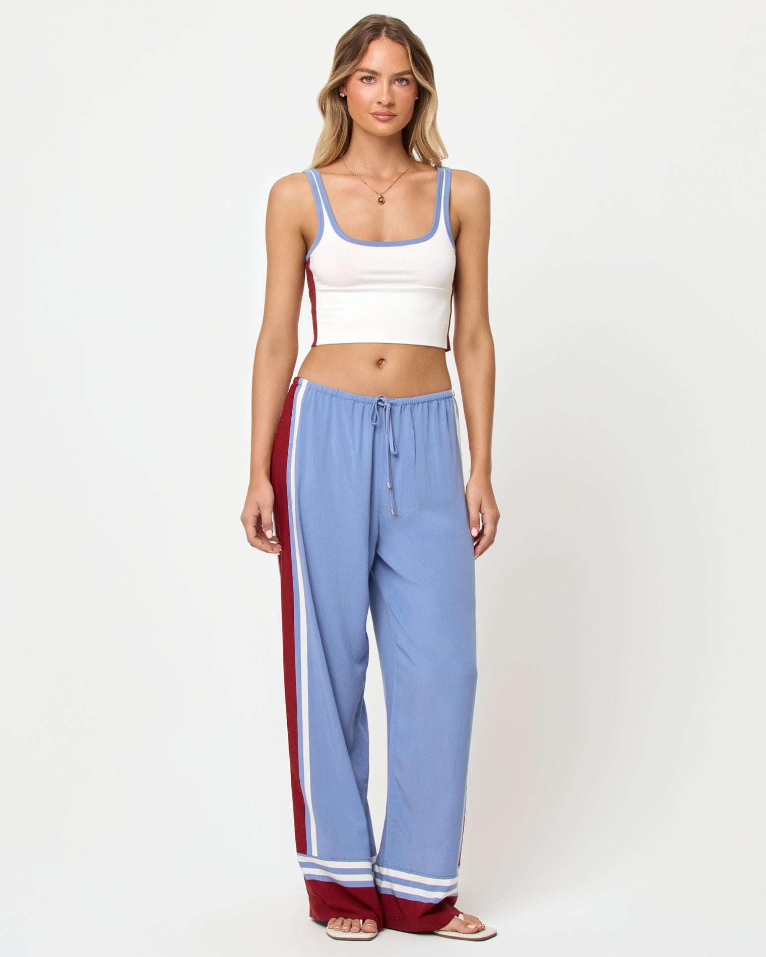 Front full-length studio view of the Reset Tank and Unwind Pant in Cream-Chambray-Fig, a cream ribbed scoop-neck crop cami with chambray blue and burgundy trim and color-block sides paired with chambray blue wide-leg stripe pants with a burgundy side stripe and cream piping, stripe trim at the ankles, styled with nude heeled sandals.