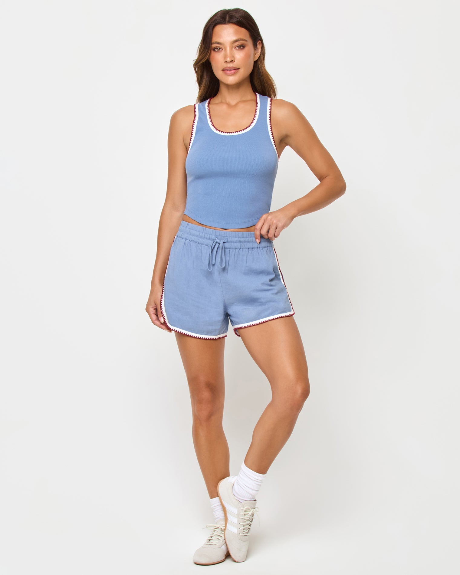 Front full-length studio view of the Ash Tank and Rune Short in Cream-Chambray-Fig, a chambray blue ribbed scoop-neck crop tank with white and burgundy crochet trim paired with matching chambray blue runner shorts with the same crochet trim, white crew socks, and cream sneakers.