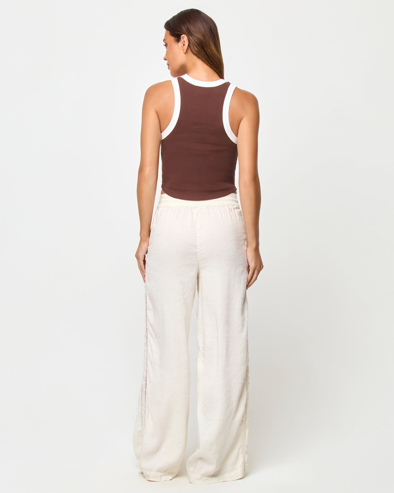 Back view of a model wearing the LSPACE Ash Tank in espresso-cream, showing the racerback detail with cream contrast trim against the espresso brown body, styled with cream wide-leg drawstring pants.