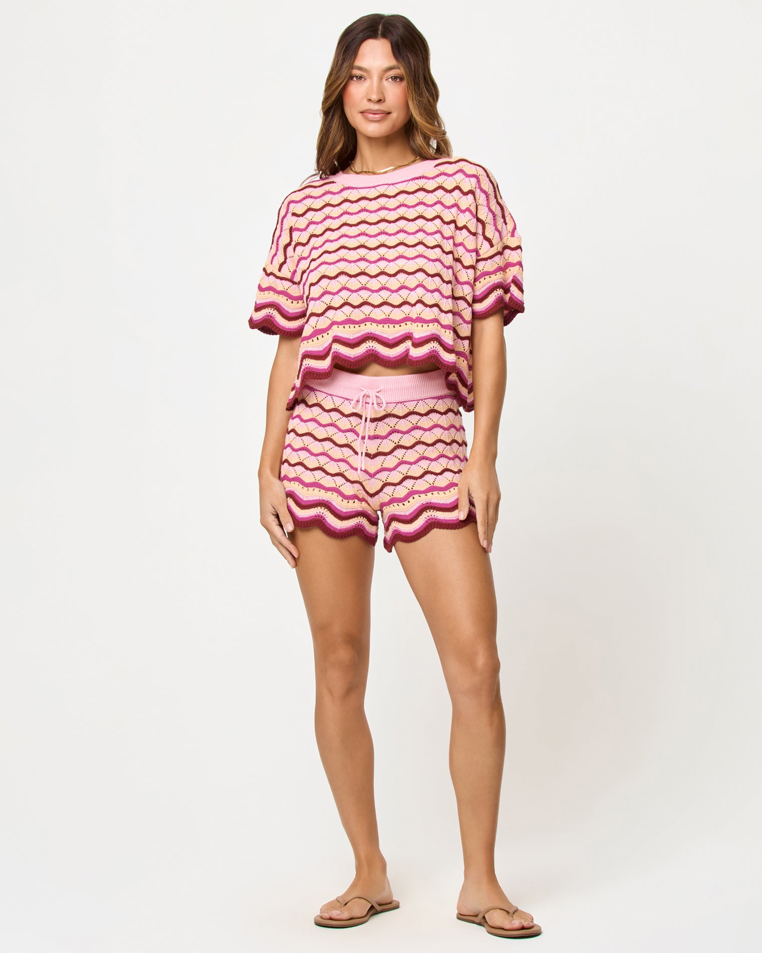 Berry Spritz | Badge:New Arrival_#B2AC88_#ffffff'
Front view of model wearing the LSPACE Sunchaser Short in berry spritz, a crochet mini short with scalloped hem in berry and pink tones, styled with matching top.