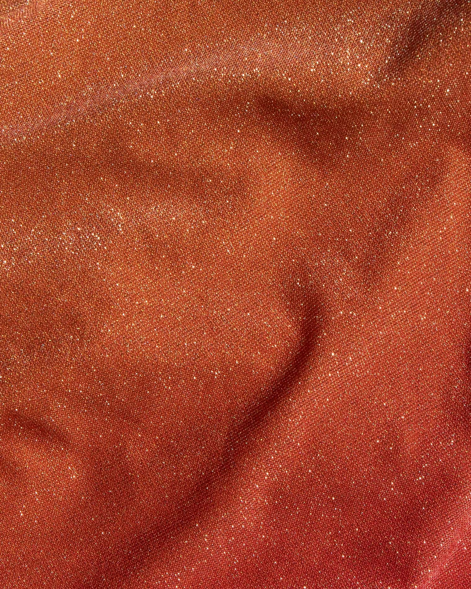 A close-up of a textured fabric with a fine glittery finish, showing a warm coppery-brown color with subtle folds and shimmer.